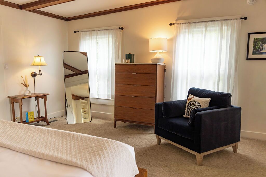 A hotel room with a bed, a dresser, a chair, a mirror, and two lamps.