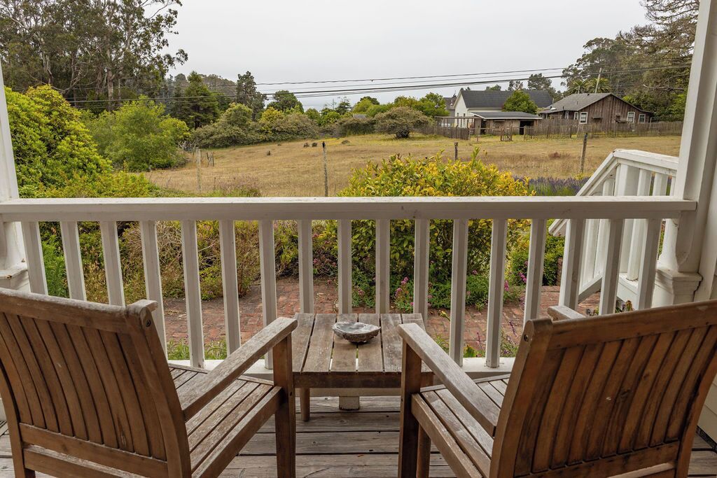Une terrasse en bois avec une balustrade blanche, deux chaises en bois et une table sur laquelle se trouve un saladier.