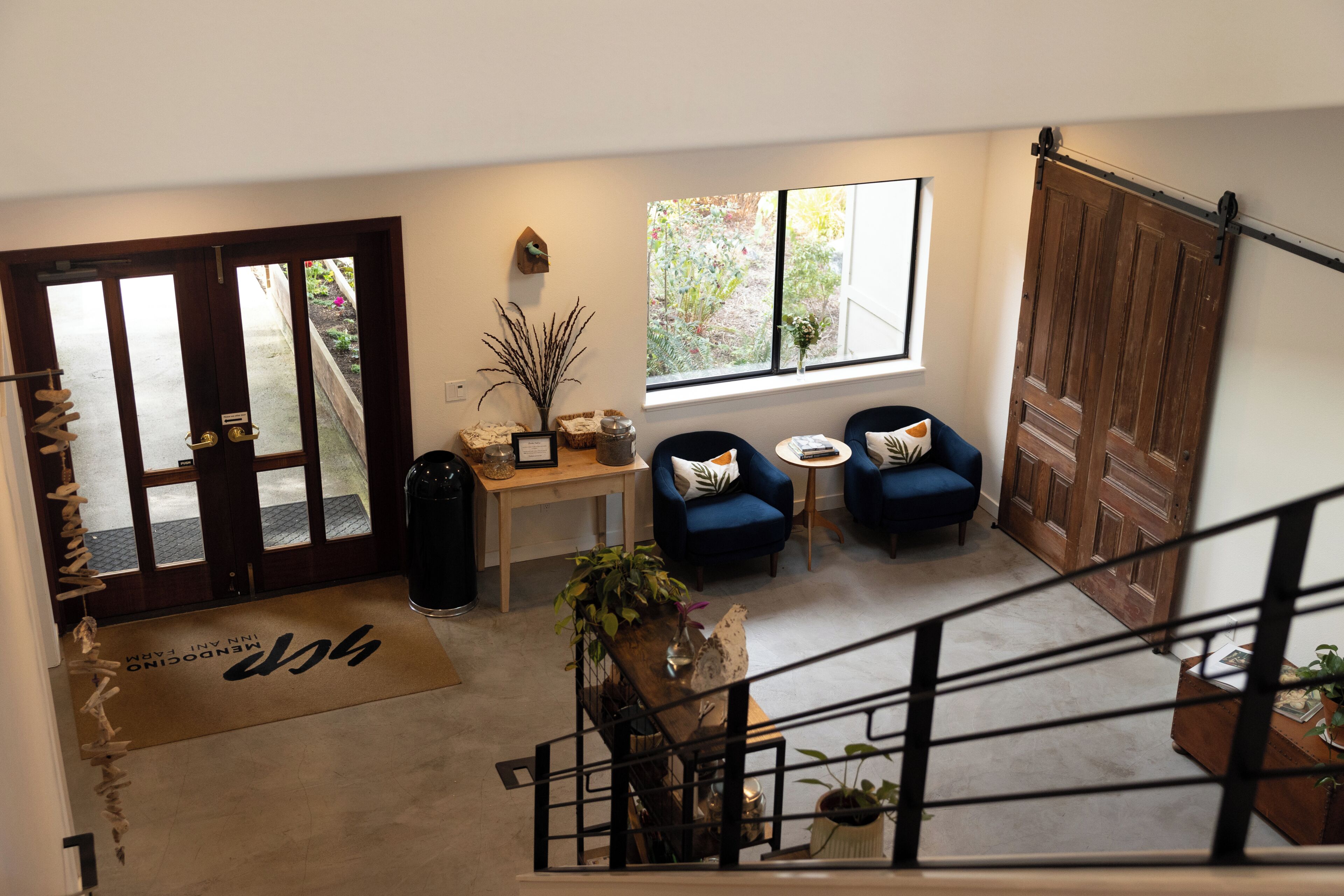 A spacious living area with a view of the garden through a large window, a wooden door, and a staircase leading to an upper level.