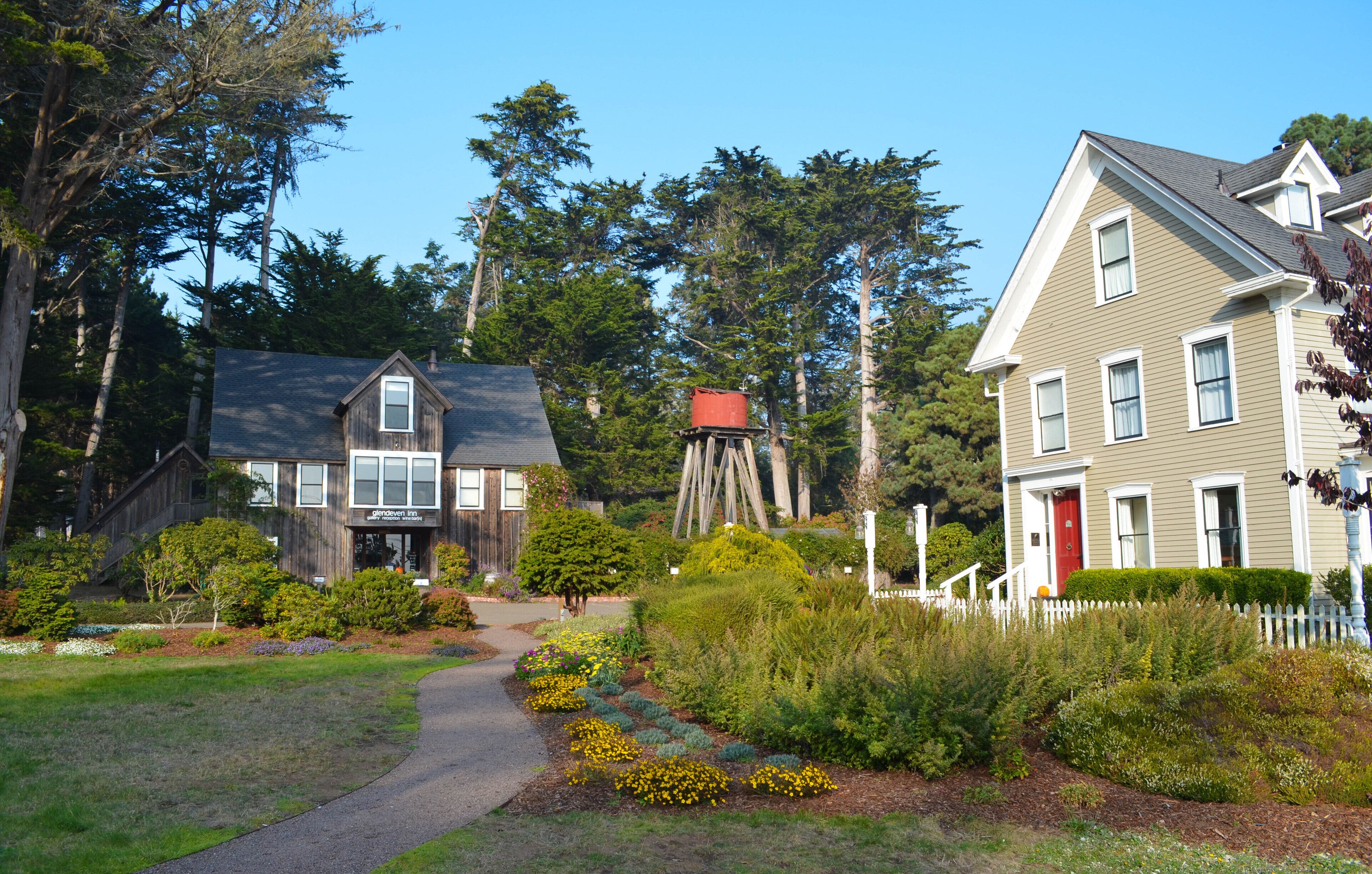 A residential area with two houses, a wooden structure, and a well-maintained garden with a pathway.