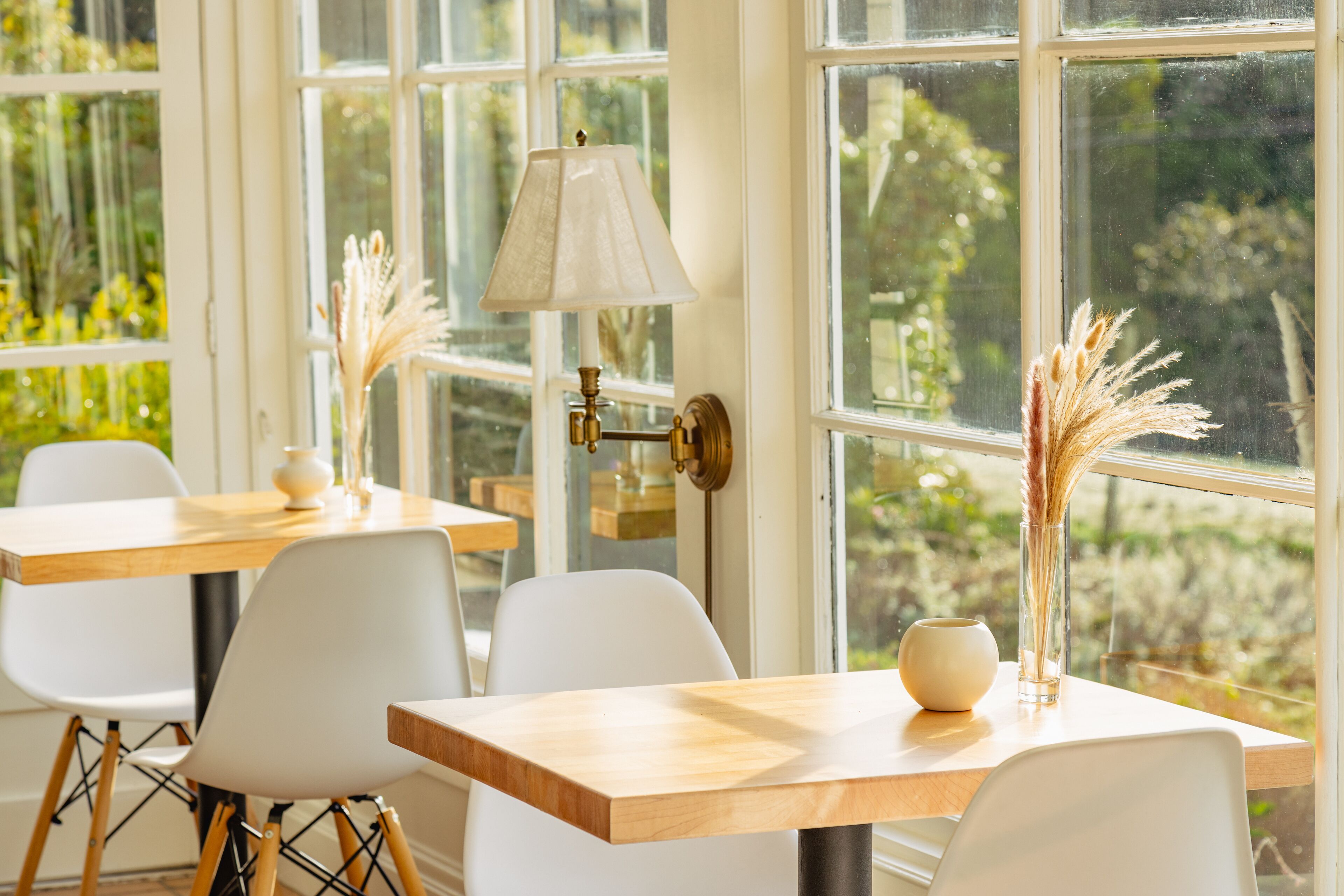 A dining area with a wooden table, white chairs, a lamp, and decorative plants.