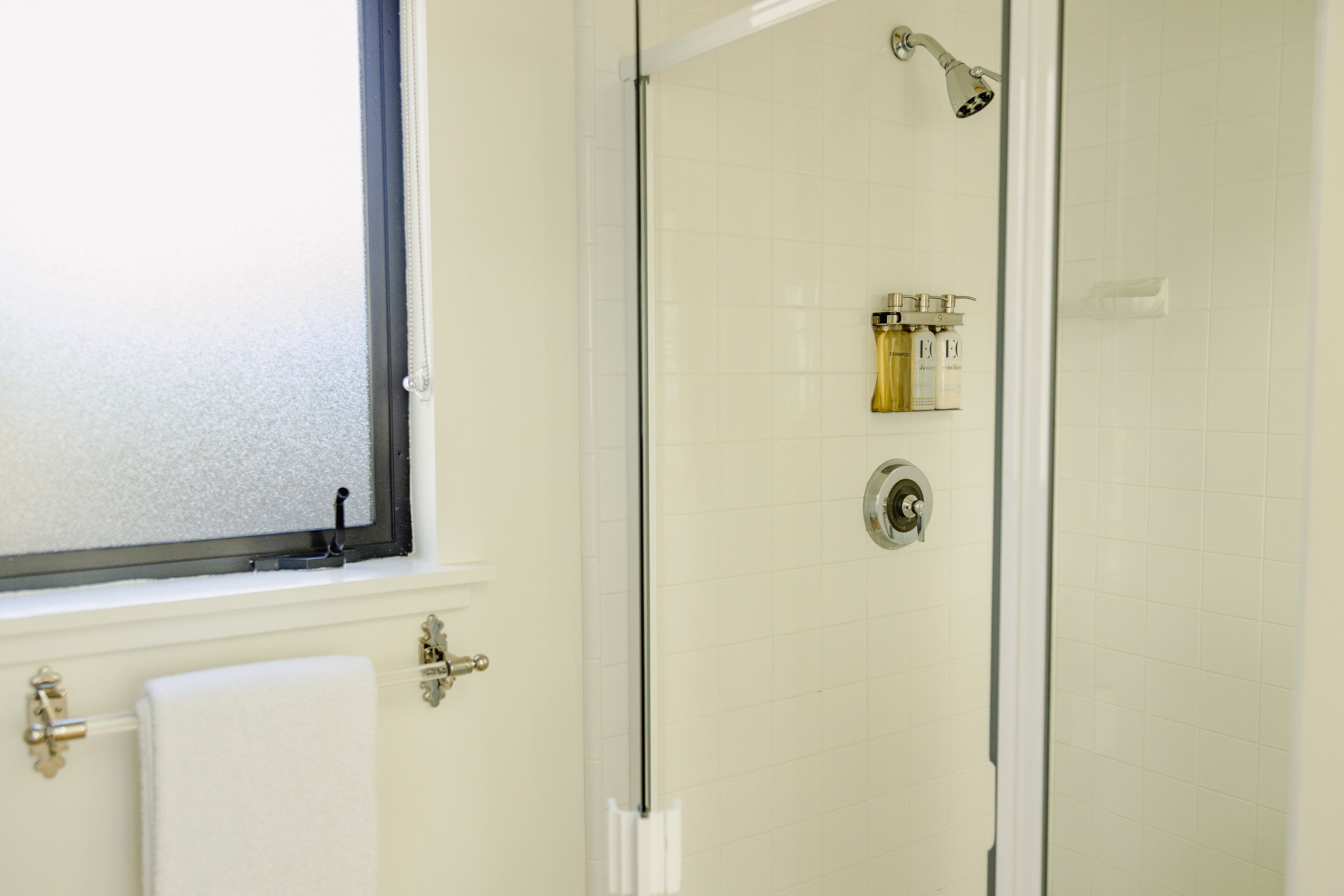 A bathroom with a glass shower door, a window, and a towel rack.