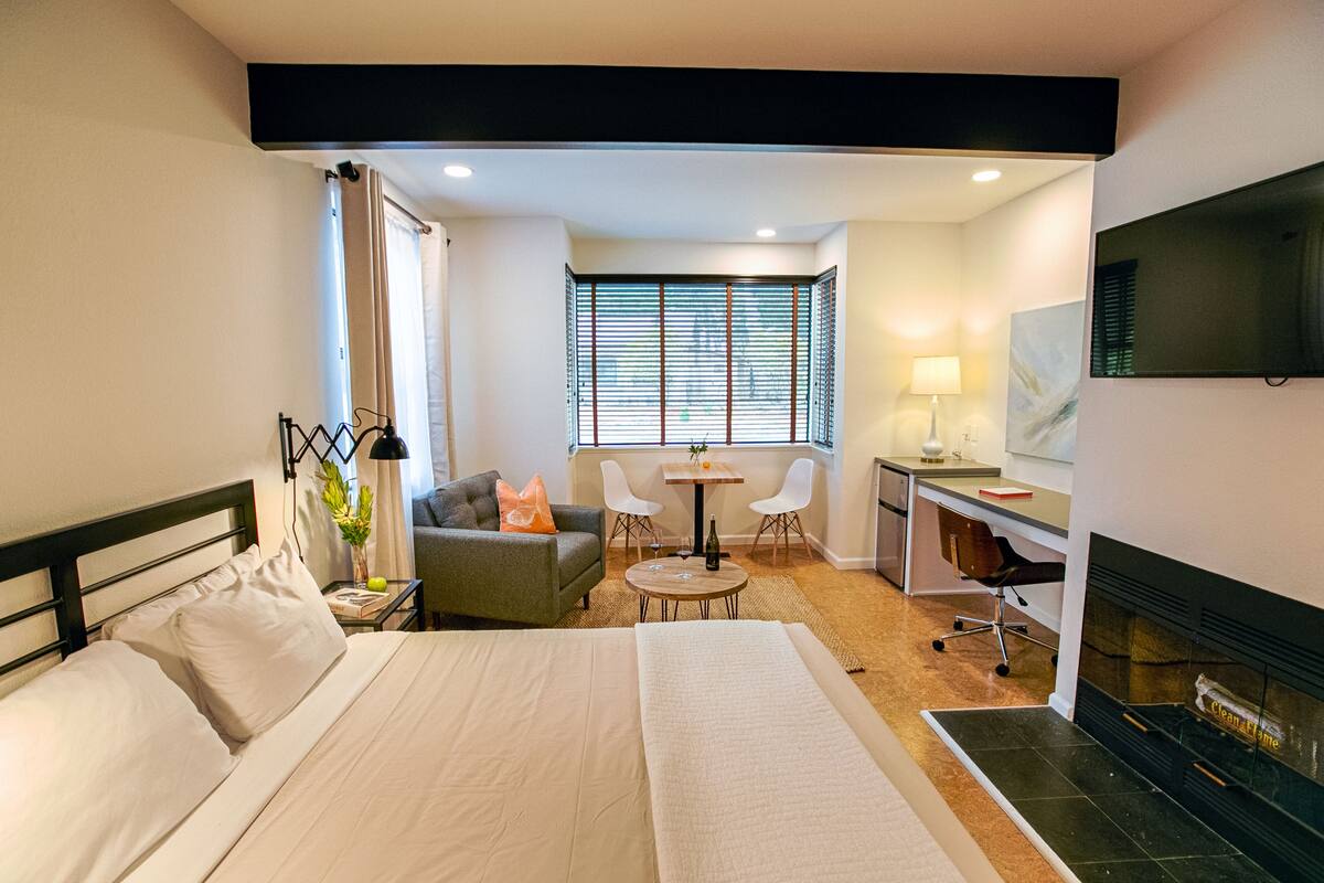 A hotel room with a bed, a desk, a chair, a TV, and a fireplace.