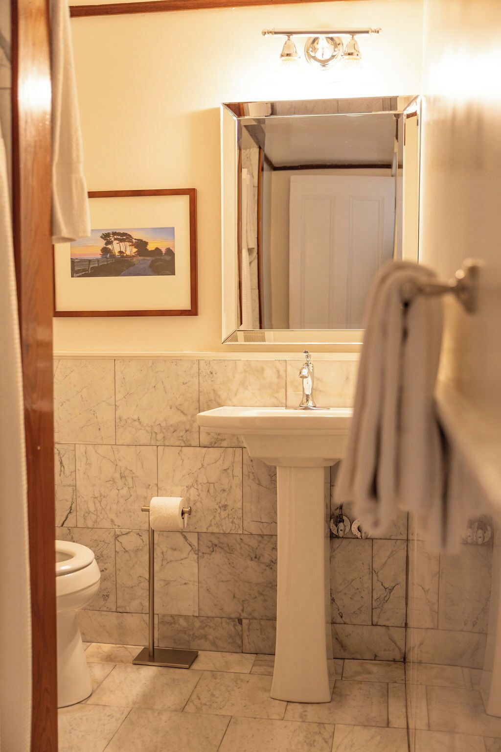 Un baño con un lavamanos pedestal, un cuadro en la pared y un perchero.