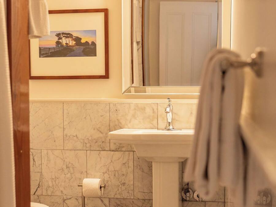 Un baño con un lavamanos pedestal, un cuadro en la pared y un perchero.