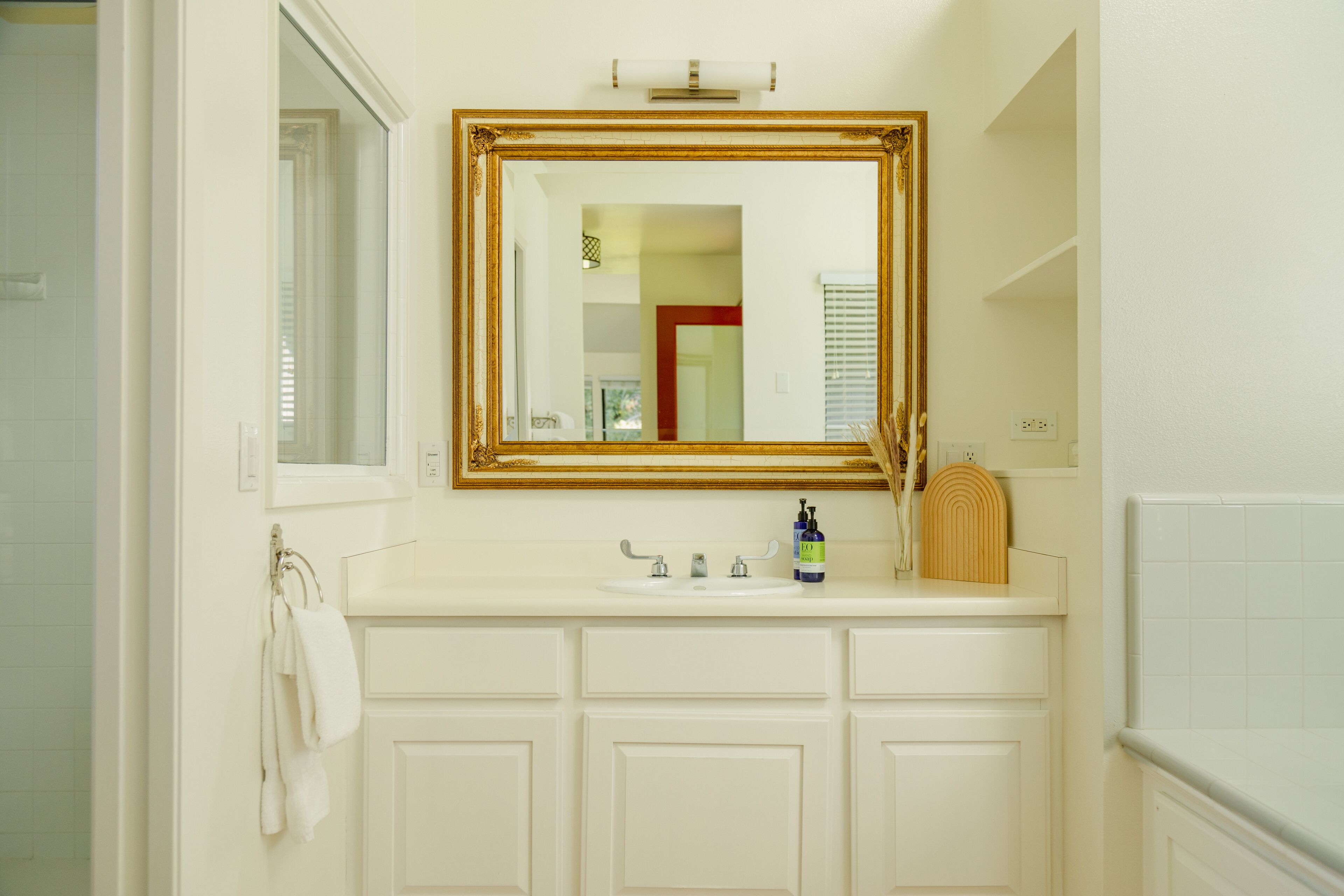 A bathroom with a white vanity, a gold-framed mirror, a sink with a faucet, and a towel rack.