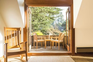 A room with a wooden chair and a table, a sliding glass door leading to an outdoor area with a view of trees. - SCP Mendocino Inn and Farm (Little River)