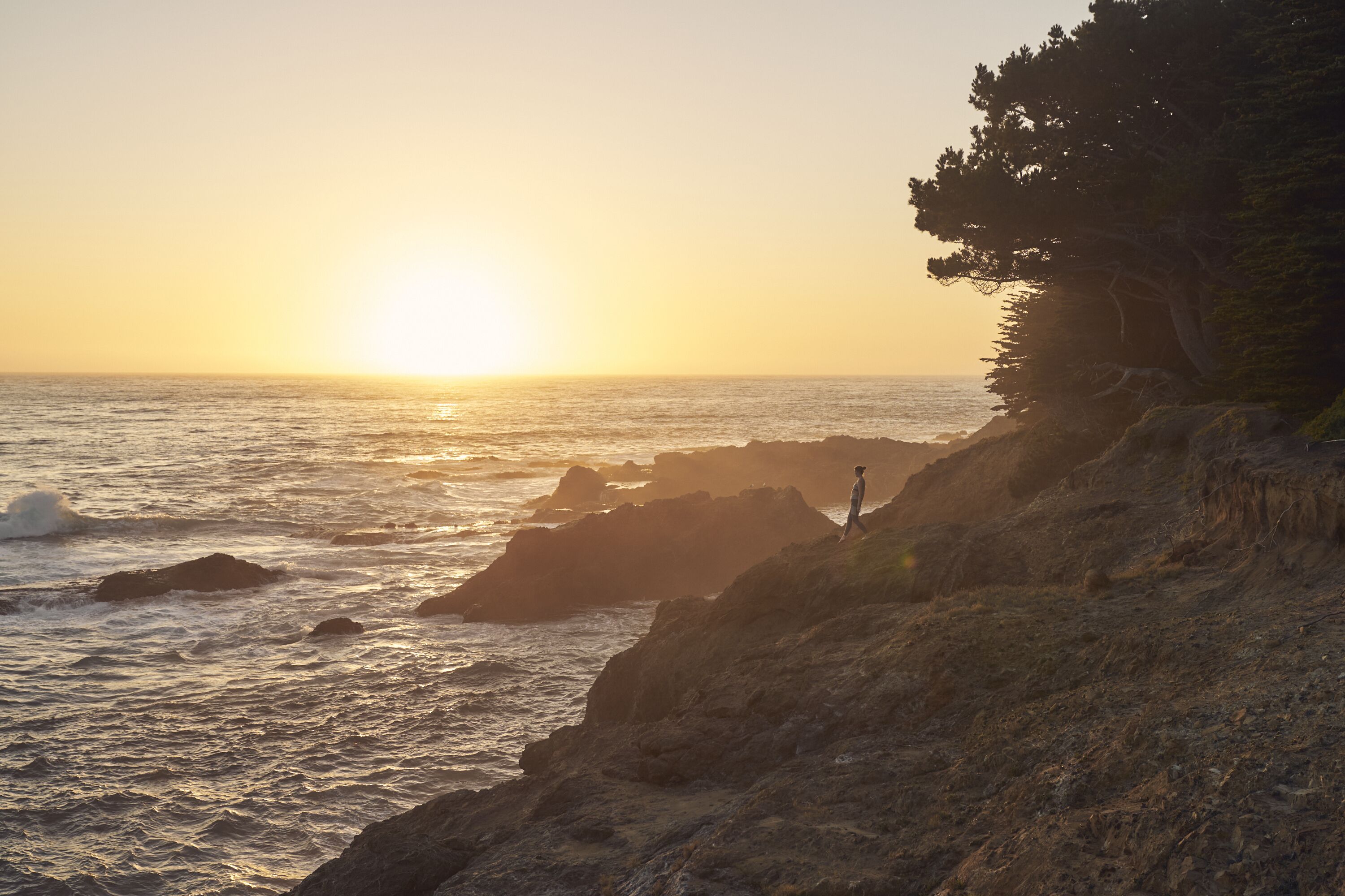 A coastal landscape with a rocky shoreline and a person standing on a cliff overlooking the ocean.