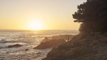 A coastal landscape with a rocky shoreline and a person standing on a cliff overlooking the ocean.