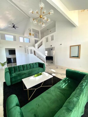 A spacious living area with a green sofa set, a white coffee table, and a modern chandelier. - Casa Nico - Contemporary Home with Pool & Gym (El Paso)
