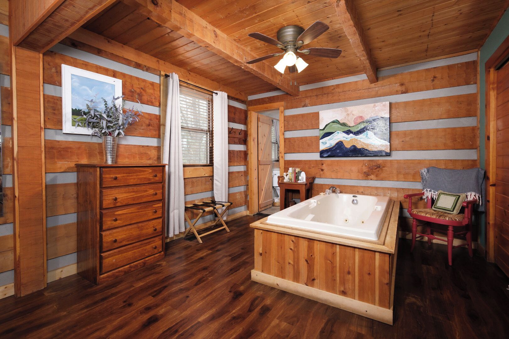 Interior de uma cabana de madeira com uma banheira grande, cômoda de madeira e ventilador de teto.