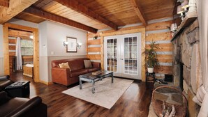 A cozy log cabin interior with a wooden ceiling, a brown leather sofa, a coffee table, and a stone fireplace. - Heaven in the Pines: Pure Bliss in the Smokies (Sevierville)