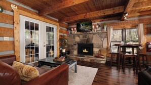 A cozy cabin interior with a stone fireplace, wooden walls, a leather sofa, and a dining area. - Heaven in the Pines: Pure Bliss in the Smokies (Sevierville)
