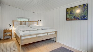 A bedroom with a wooden bed, white walls, a nightstand with a lamp, and a painting on the wall. - 3 bedroom cozy home in Nykøbing Sj (Nykøbing Sj)