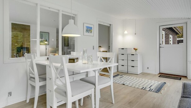 A modern, white-themed dining area with a large table and chairs, pendant lights, and a view of the outside through large windows. - 3 bedroom cozy home in Nykøbing Sj (Nykøbing Sj)