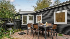 A patio with a table and chairs, a grill, and a wooden fence. - 3 bedroom cozy home in Nykøbing Sj (Nykøbing Sj)