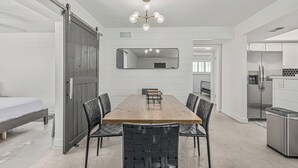 Una cocina moderna con un refrigerador de acero inoxidable, una mesa de comedor de madera con sillas negras, y un espejo grande sobre la mesa.