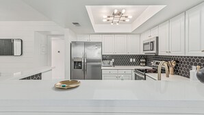 Una cocina moderna con armarios blancos, un refrigerador de acero inoxidable, un microondas y un salpicadero con baldosas blanco y negro.