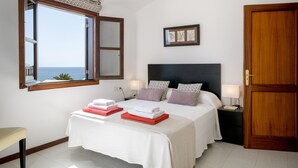 Une chambre avec une grande fenêtre, un lit sur lequel sont soigneusement pliées des serviettes, une table de chevet avec une lampe et un tableau encadré accroché au mur.