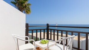 Un balcon avec des chaises blanches et une table, donnant sur une plage et la mer.