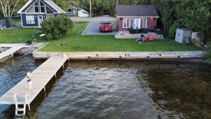 Un quartier résidentiel avec une jetée qui s’avance dans l’eau, une voiture rouge garée sur la pelouse et une maison dotée d’un porche.