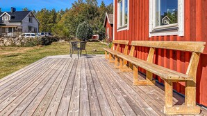 Um deck de madeira com bancos, uma mesa e cadeiras, que leva a um edifício vermelho com uma janela.
