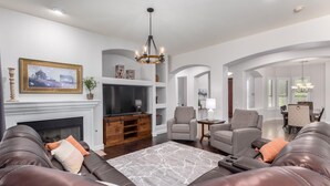 A spacious living room with leather sofas, a fireplace, a TV, and a chandelier.