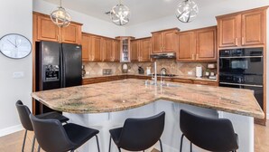 A modern kitchen with a granite island, wooden cabinets, stainless steel appliances, and pendant lighting.