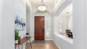 A hallway with a wooden door, a painting, a potted plant, a bench, and a dining area with a chair.