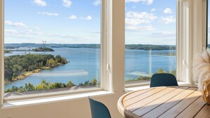 Ein Zimmer mit großem Fenster und Blick auf einen See sowie Stromleitungen in der Ferne.