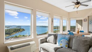 Ein Wohnzimmer mit großem Fenster mit Seeblick, einem Deckenventilator und einem Essbereich mit blauen Stühlen.