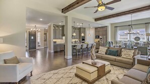 A spacious living room with a large sofa, a coffee table, and a fluffy rug. There is a kitchen area with modern appliances and a dining area with chairs. - Family-Friendly Brookshire Home w/ Game Room! (Brookshire)