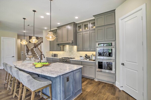 A kitchen with a central island, bar stools, a stove, and a refrigerator.