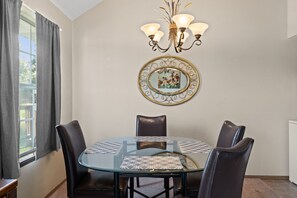 Un coin repas comprenant une table ronde en verre, quatre chaises, un lustre et un tableau encadré accroché au mur.