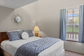 Un lit bien fait, avec une literie à motifs, une lampe de chevet et un miroir géométrique accroché au mur.