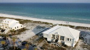 A beachfront property with a large house and a smaller building, both featuring white exteriors and a sandy beach in the background. - Amazing Views! Elegant Gulf Front Home: Elevator, Huge Deck/Walkover, Beach Gear (Pensacola Beach)