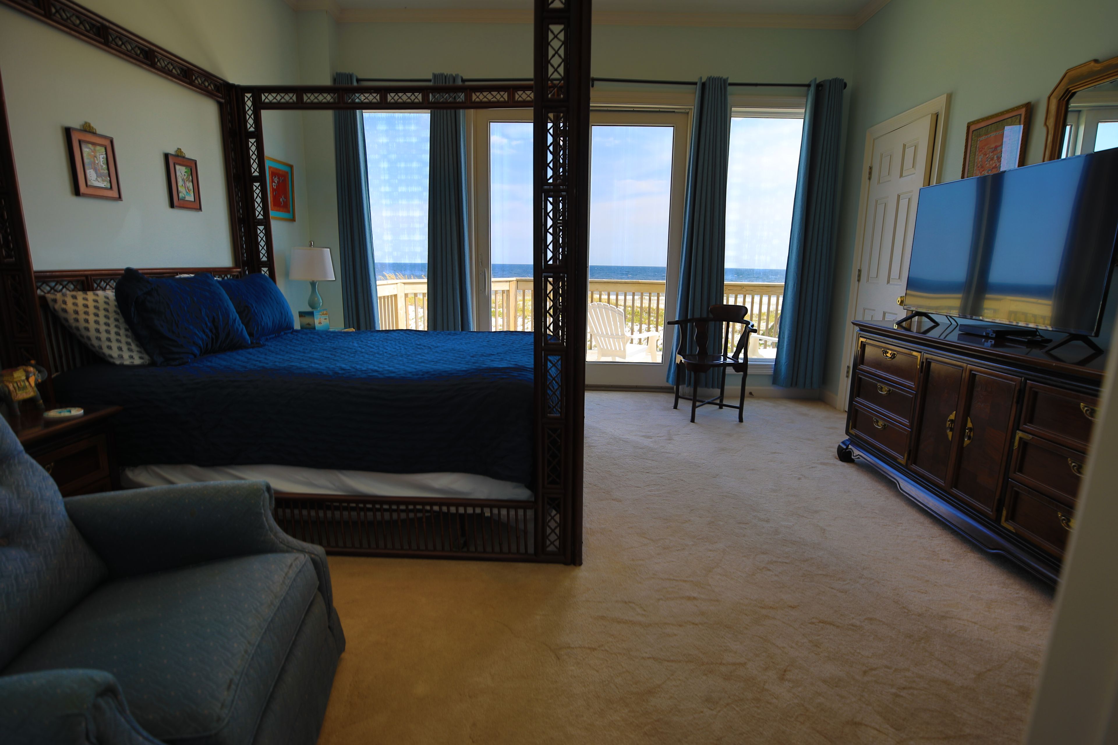 A bedroom with a four-poster bed, a television, and a view of the ocean.