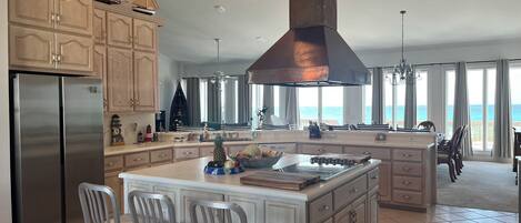 A spacious kitchen with a large island, wooden cabinets, and a view of the ocean.