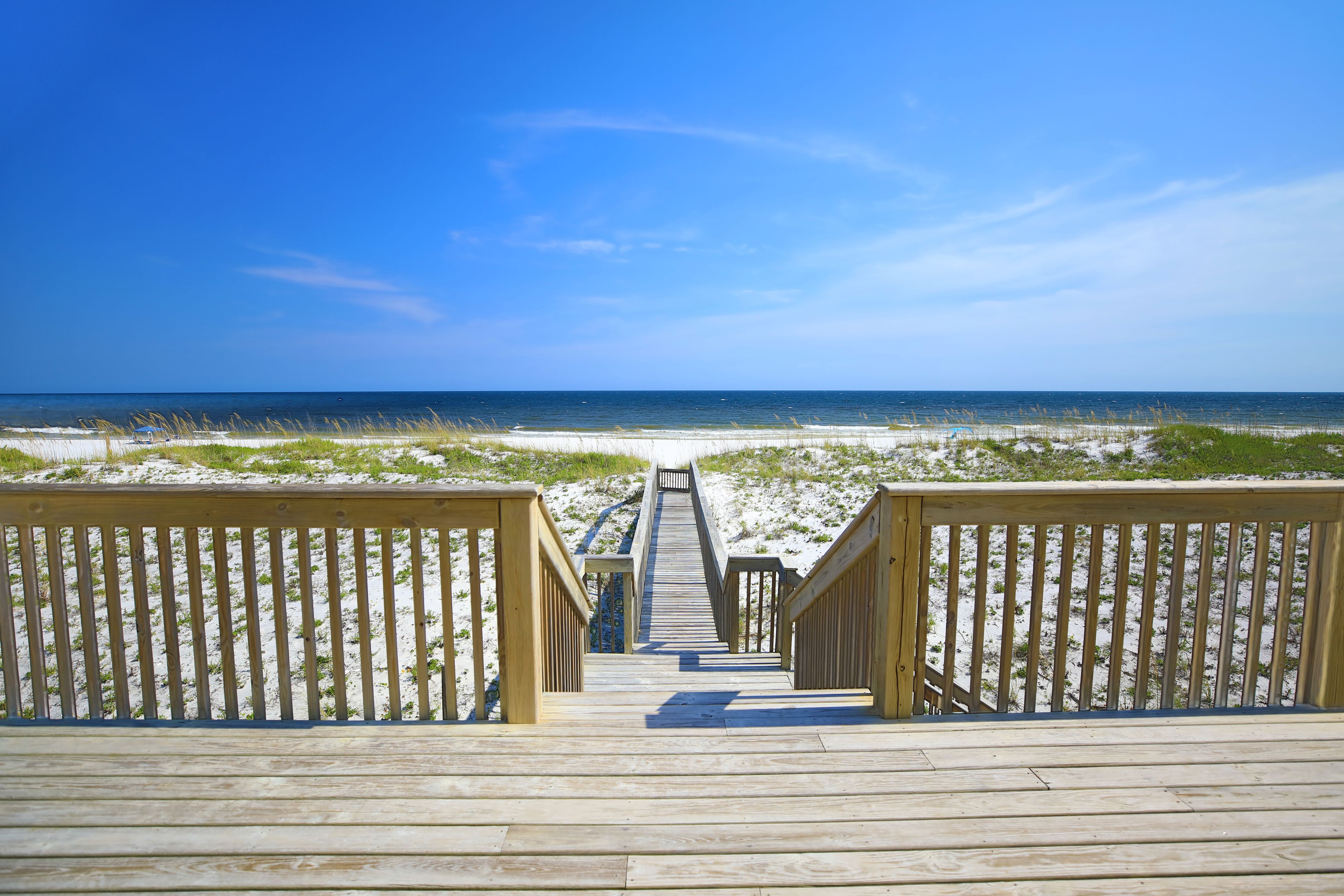 A wooden boardwalk leading to a beach with clear skies.