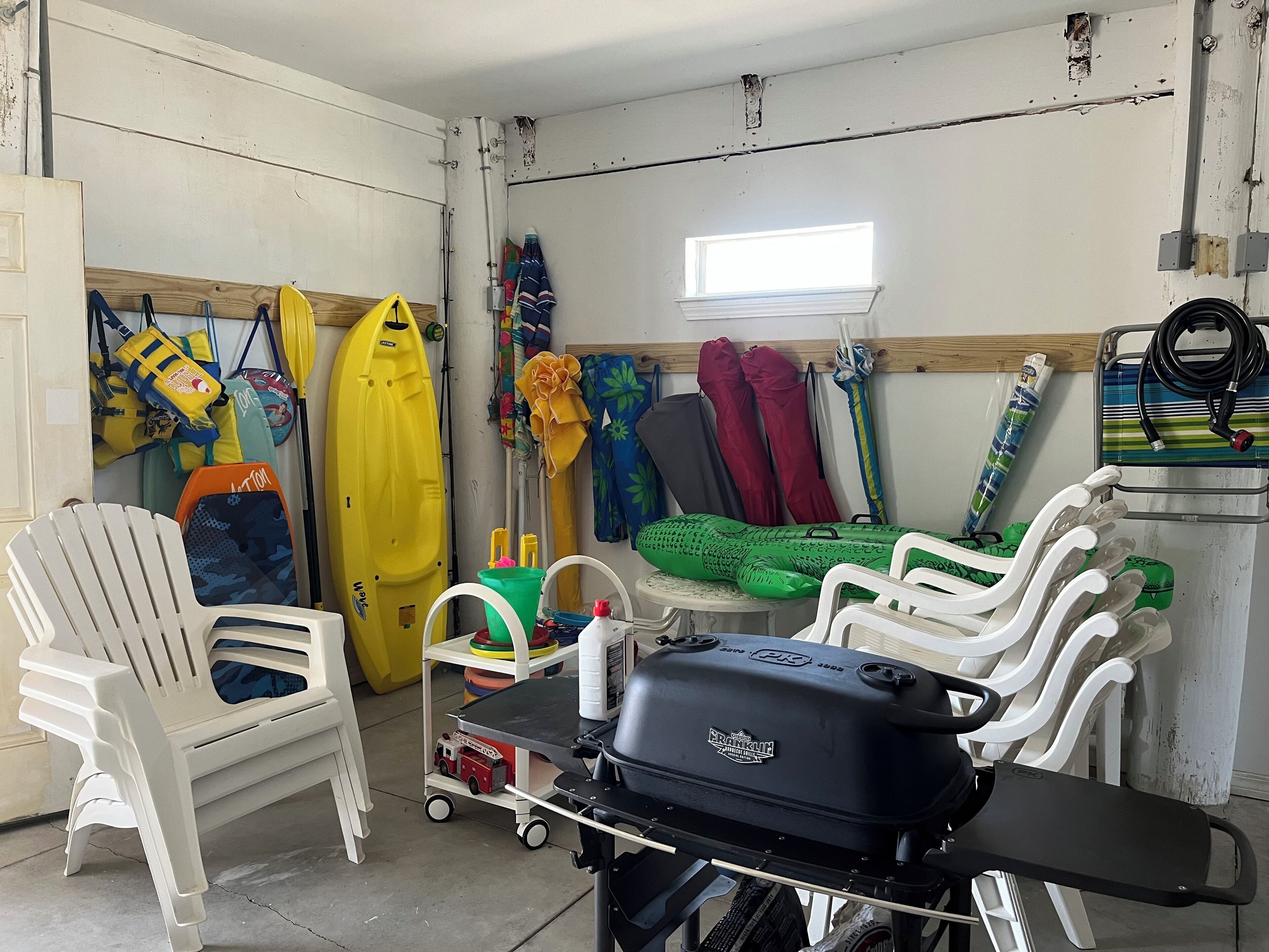 A room with white plastic chairs, a barbecue grill, and various outdoor gear like kayaks and life jackets.