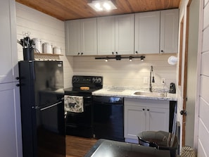 Compact kitchen with a refrigerator, stove, sink, and microwave, featuring white cabinets and a window.