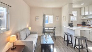 Un appartement moderne comprenant un salon, un coin repas et une cuisine. On y trouve un canapé, une table à manger avec des chaises, ainsi qu’un comptoir de cuisine avec des tabourets.