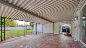 Un espacio al aire libre techado, con suelo de hormigón, barandillas de metal y vista a un jardín.