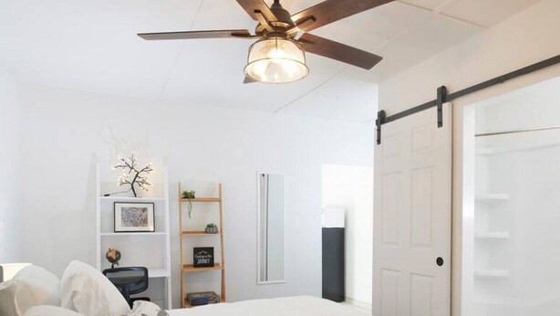 Un dormitorio con una cama grande, un ventilador de techo, un armario y un escritorio con una silla.