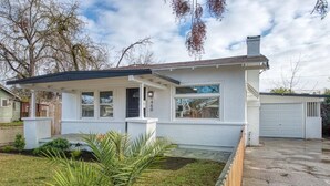 Una casa de una planta con un porche cubierto, un garaje y un césped bien cuidado con una palmera.