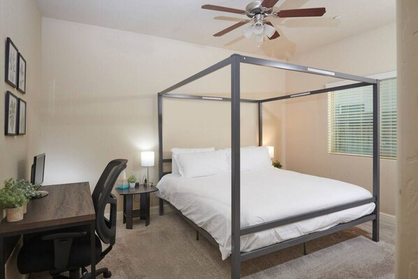 A four-poster bed with a desk and chair, a ceiling fan, and a window with blinds. - Sparkling & New KING I Close to Necessities (Fresno)