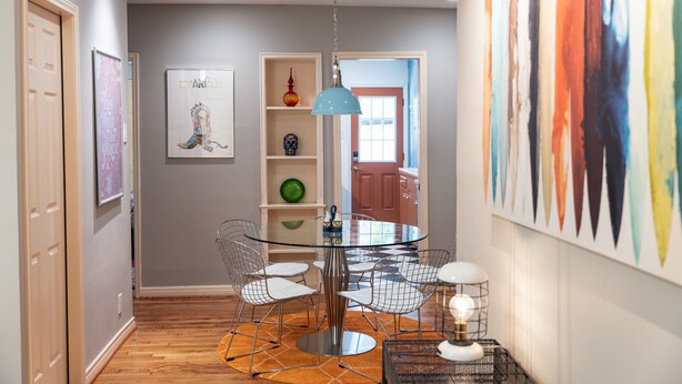 A dining area with a glass table surrounded by wire chairs, a blue pendant light, and a patterned rug. - Modernized Retro Home In The Montrose (Houston)