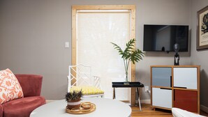 A living room with a red sofa, a white table with a plant, a yellow and white chair, a TV on the wall, and a wooden cabinet. - Modernized Retro Home In The Montrose (Houston)