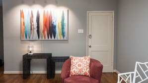 A room with a grey wall, a white door, a black console table, a red armchair, and a colorful abstract painting. - Modernized Retro Home In The Montrose (Houston)