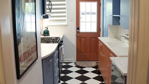 A narrow kitchen with a black and white checkered floor, blue cabinets, and a wooden door. - Modernized Retro Home In The Montrose (Houston)